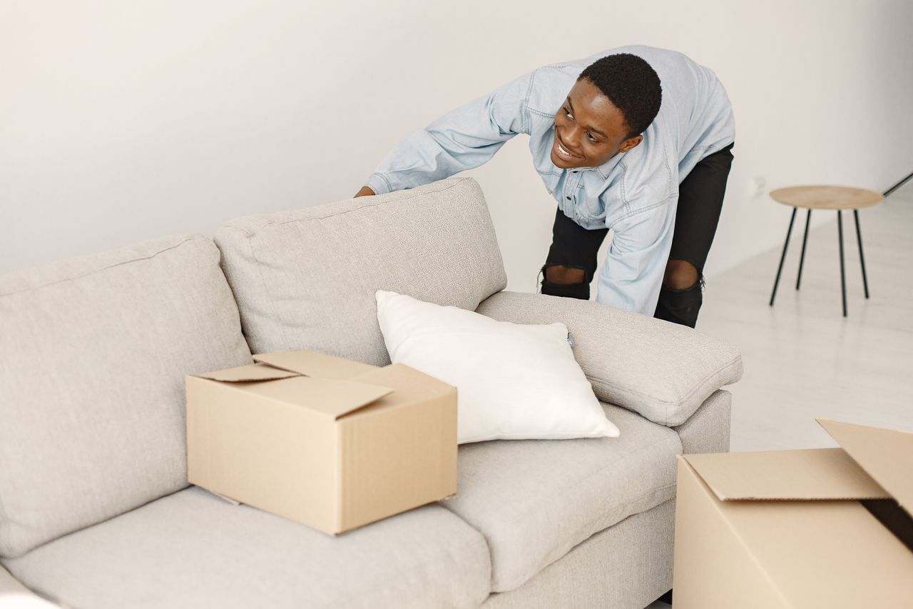 Jeune homme souriant en train d’ordonner des cartons dans un salon moderne.